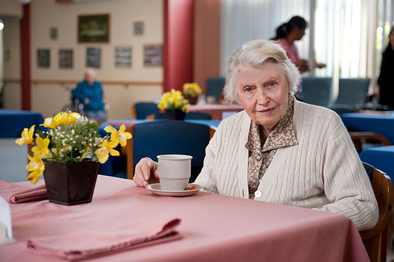 Lady with tea and yellow flowers on table at Kalyna Care