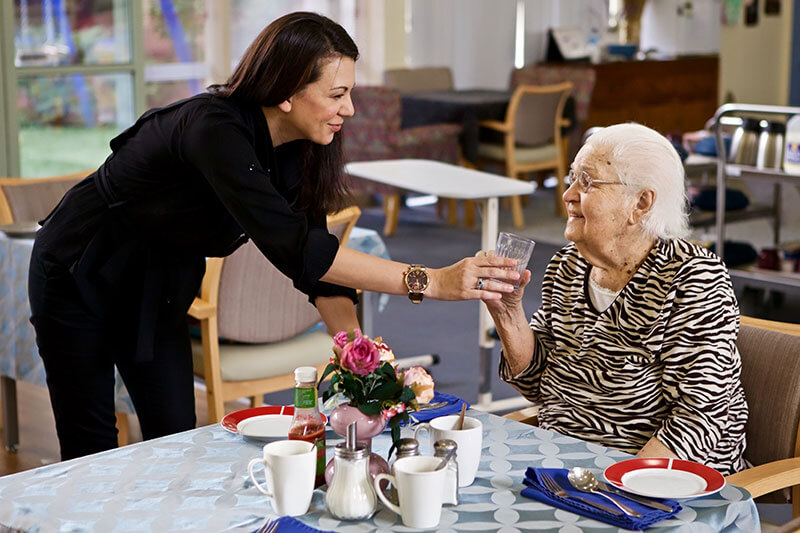 Carer offering a lady a drink of water at Kalyna Care
